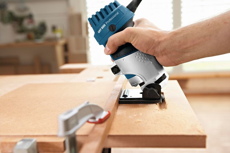 Eine Person verwendet eine Handfräse, um die Kante eines Holzbretts zu formen., Kantenfräse, Elektrowerkzeug, blau-silber, Holzbearbeitung