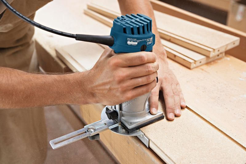Eine Person verwendet eine Handfräse, um die Kante eines Holzbretts zu formen., Oberfräse, Elektrowerkzeug, Holzbearbeitung, Kabelgebunden, Blau und silber